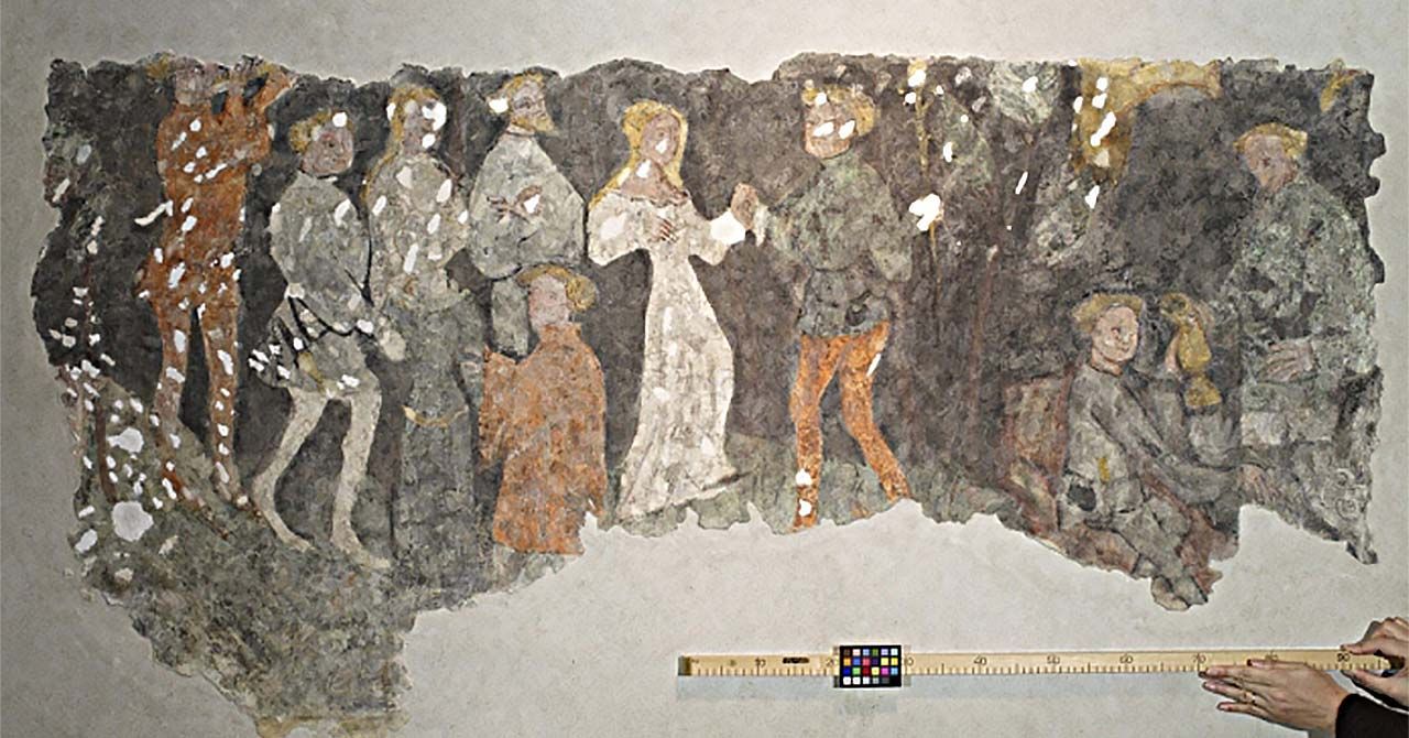 一幅壁画的很大一部分展示了一群人，中间一男一女手牵着手。一个人在壁画下面举着一根木棍。标尺上有一个小的颜色匹配网格。
