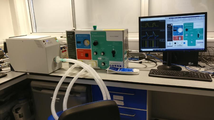 在办公室桌上,测试配置包括一个手语- 5000人工肺(左)和两个呼吸管连接到呼吸机(中间)。个人电脑右边是运行一个半实物的仿真软件模型测试。万博1manbetx